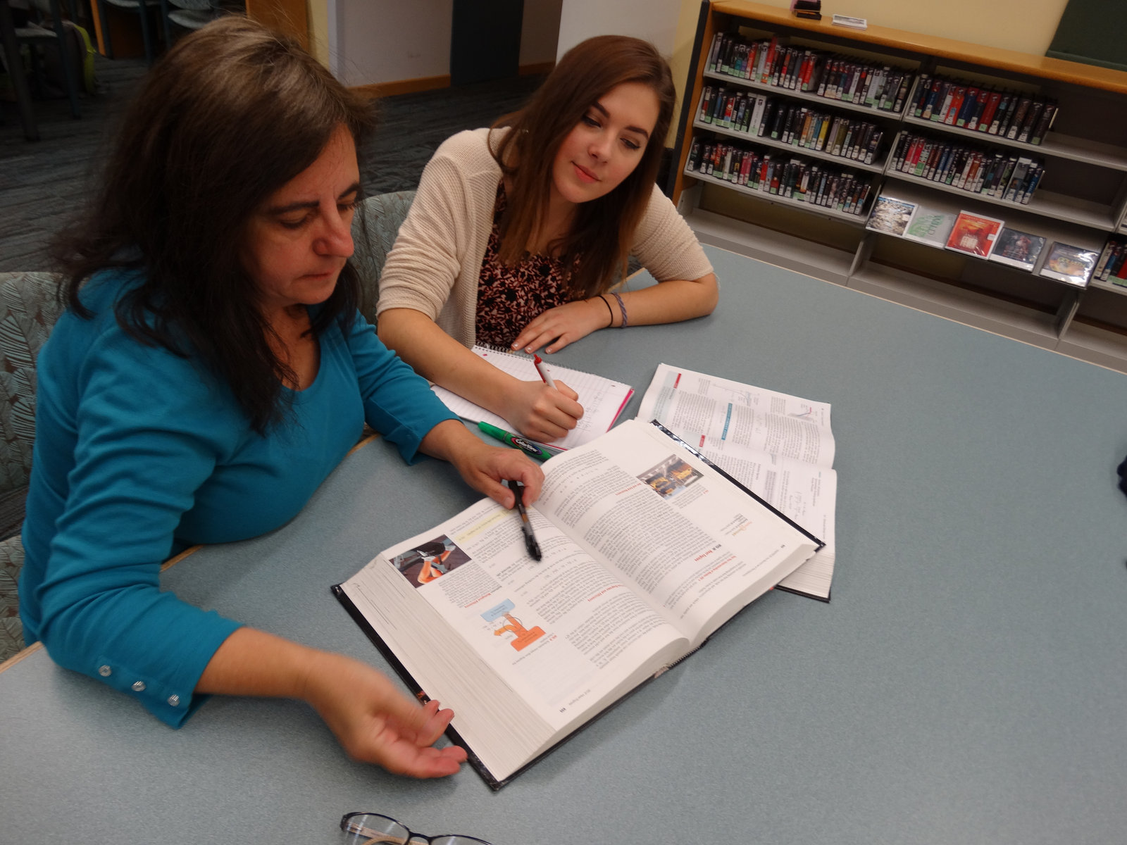 Anna tutoring a college student with a textbook in a library